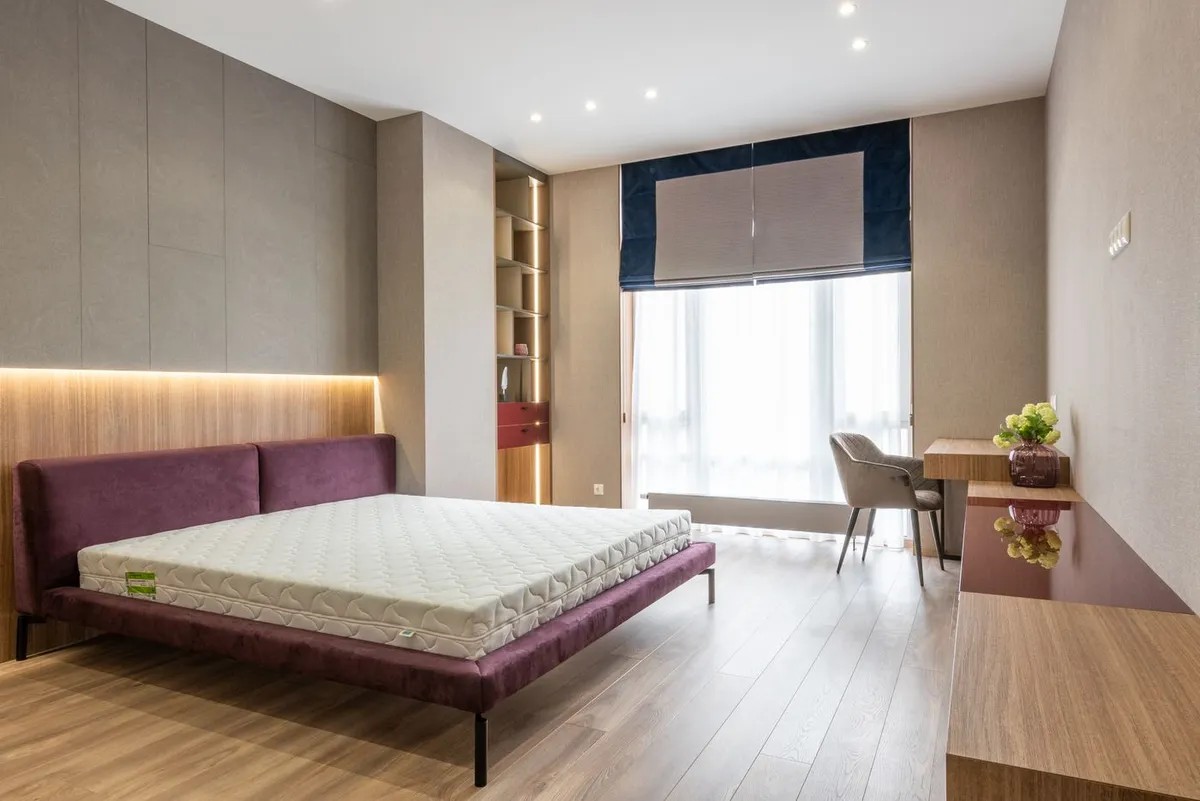 A mattress ready for storage A bare mattress on an upholstered bed frame in a bright, empty bedroom