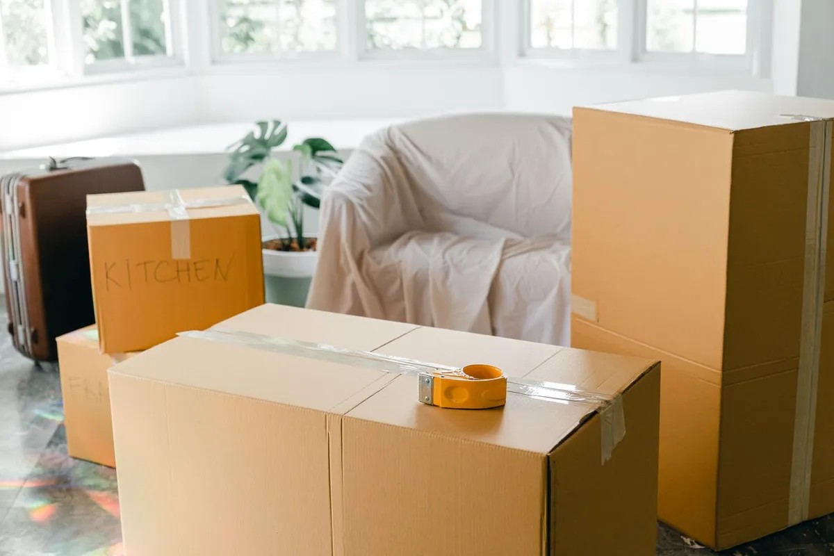 Furniture wrapped and boxed for storage An armchair covered with a white sheet next to stacked cardboard boxes in a bright room